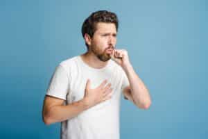 Portrait of a young man coughing against a blue background, representing immune health concerns and potential benefits of peptide therapy in wellness care